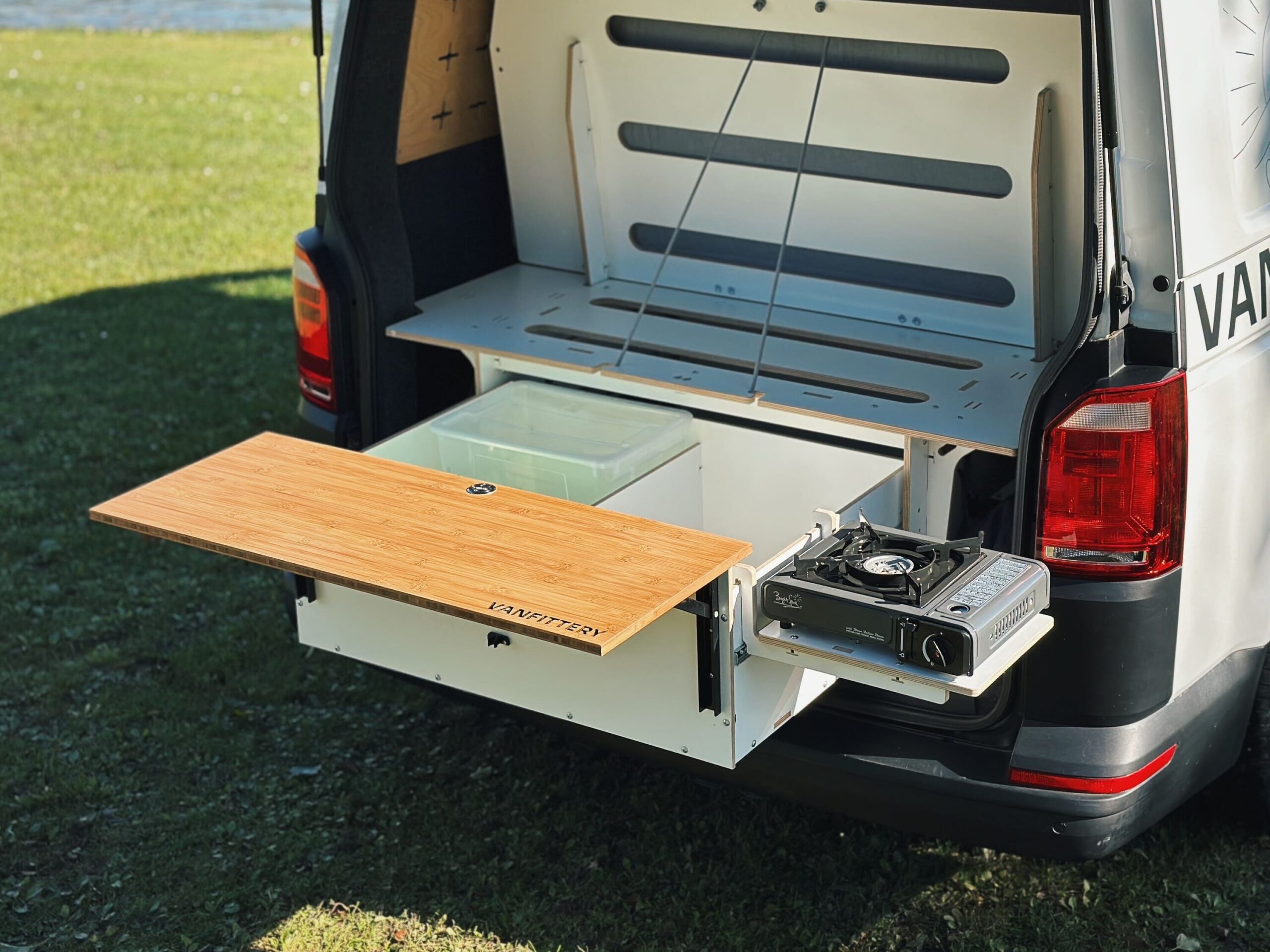 Rozkládací kuchyňský modul s dřevěným povrchem a plynovým vařičem instalovaný v zadní části obytného vozidla.