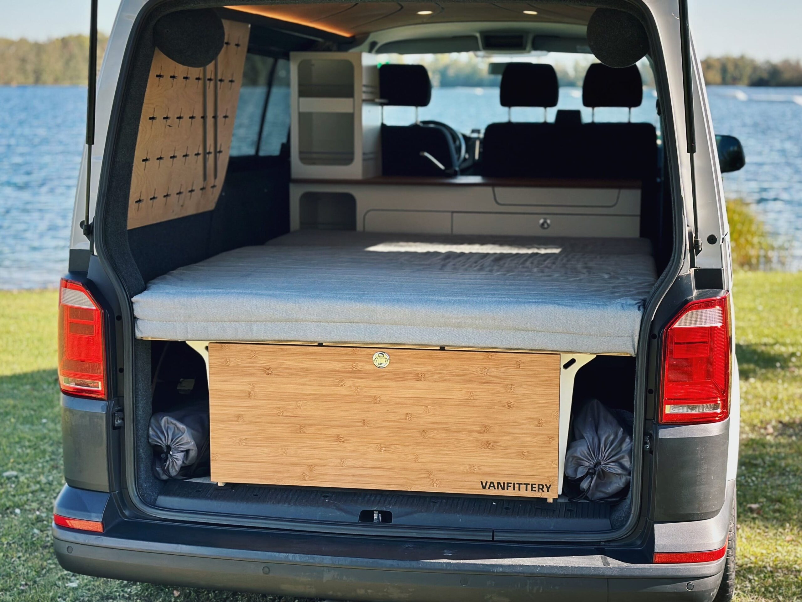 Interiér kempinkového vozidla ukazuje přestavěný spací systém s pohodlnou matrací a dřevěným modulem pro optimální využití úložného prostoru.
