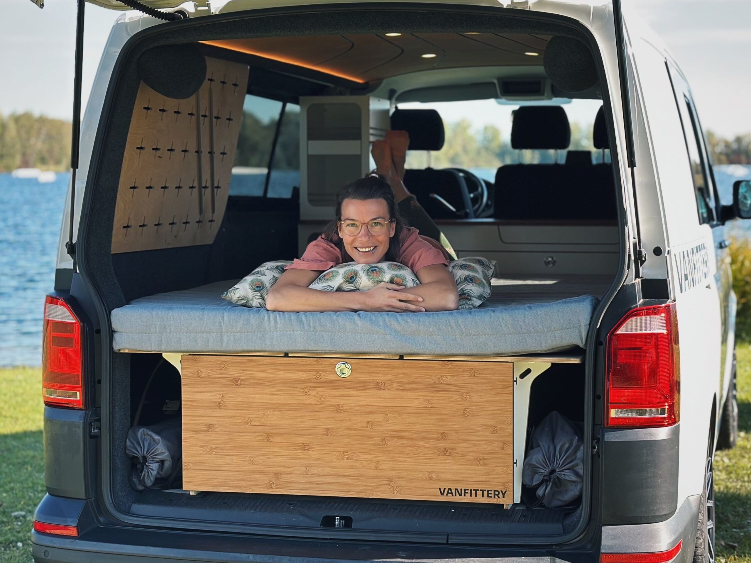 Osoba leží uvolněně na spacím systému v zavazadlovém prostoru dodávky.