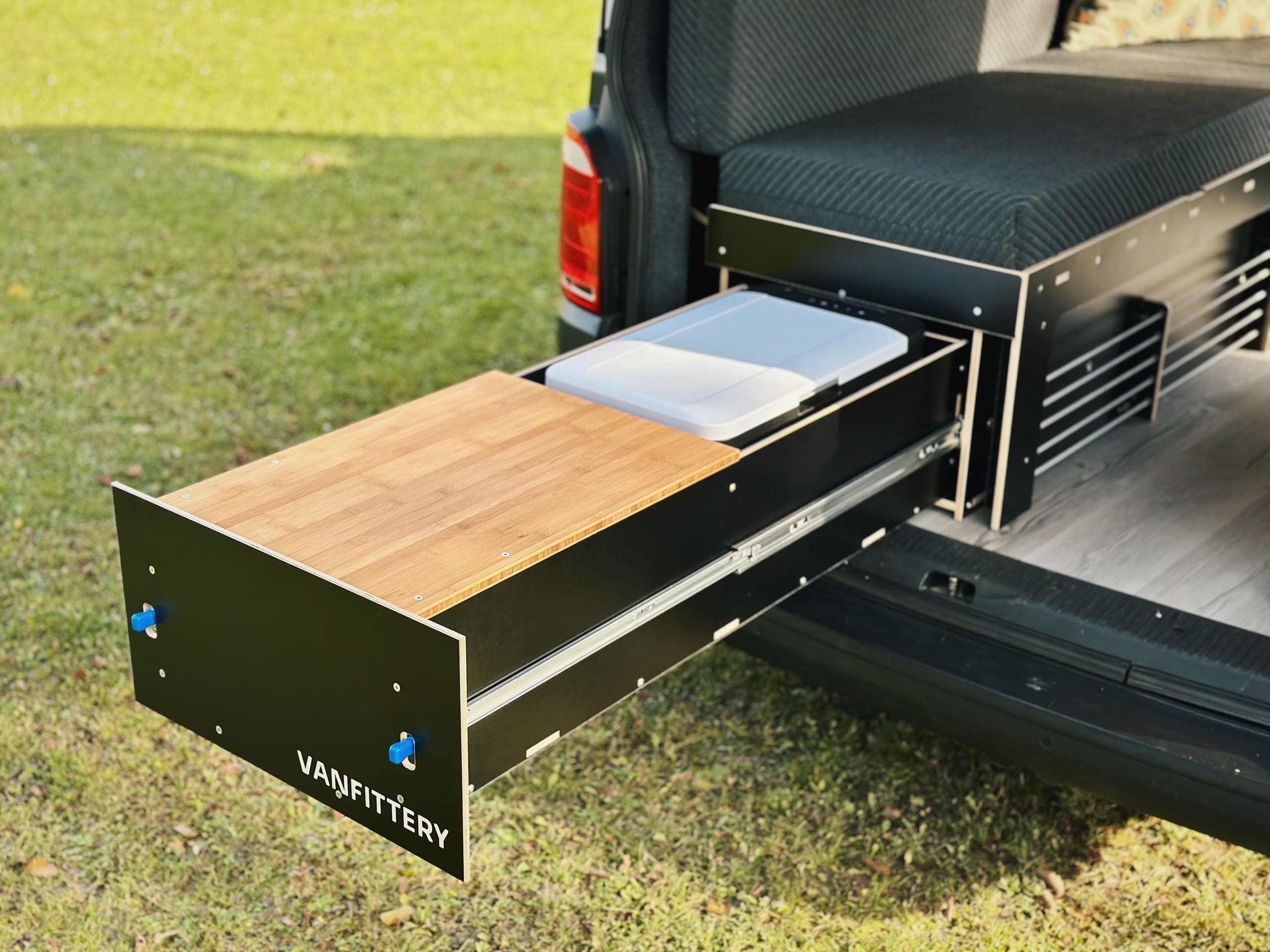 Cajonera extraíble con superficie de madera que se monta en un vehículo y forma parte de un sistema de mobiliario de camping.