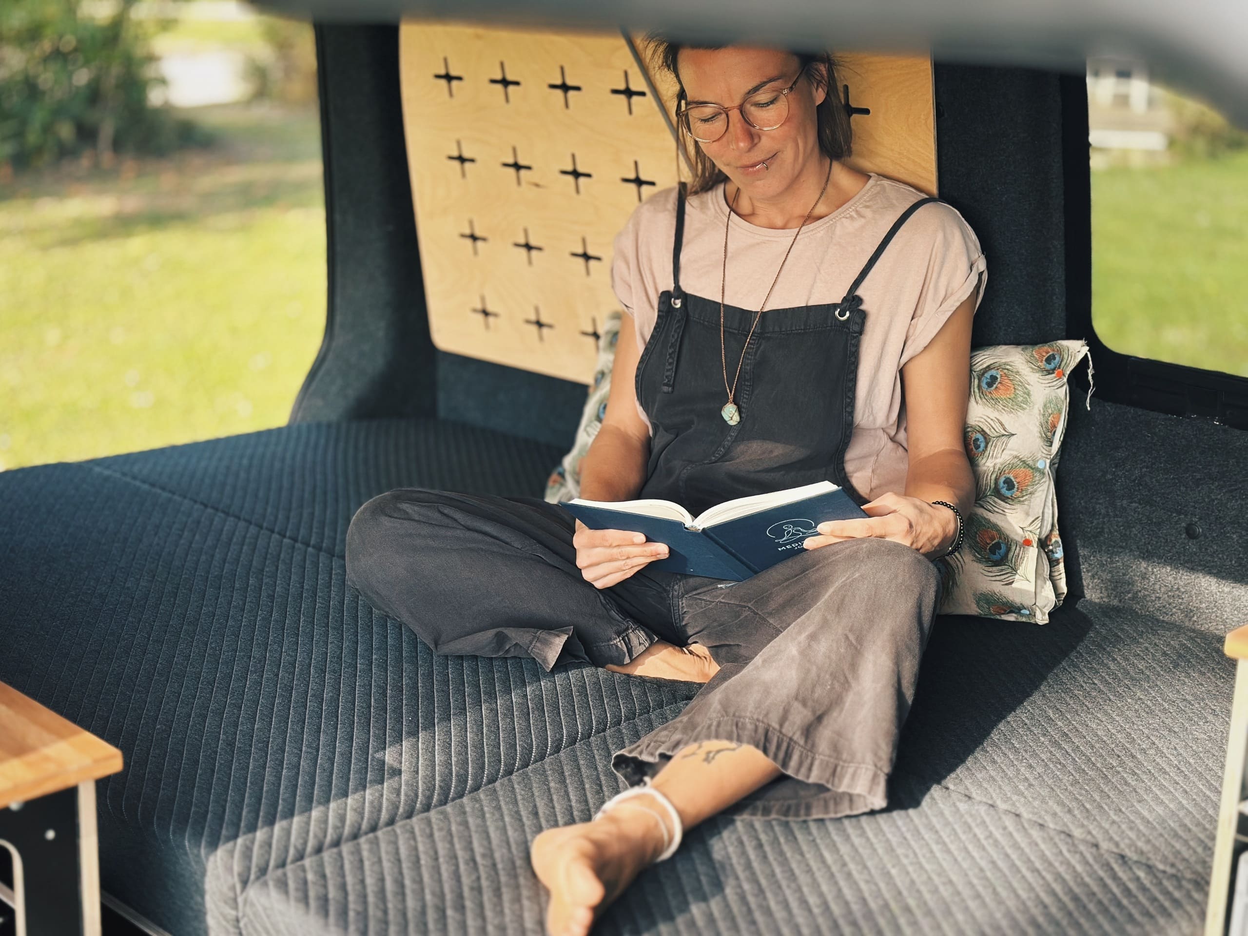 Una persona se sienta relajadamente en una cama de camping y lee un libro.