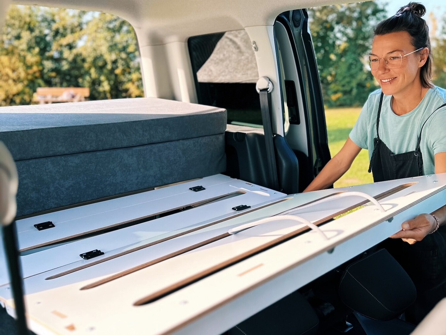 Kobieta instaluje system spania w kamperze, a w tle widać zieloną łąkę.