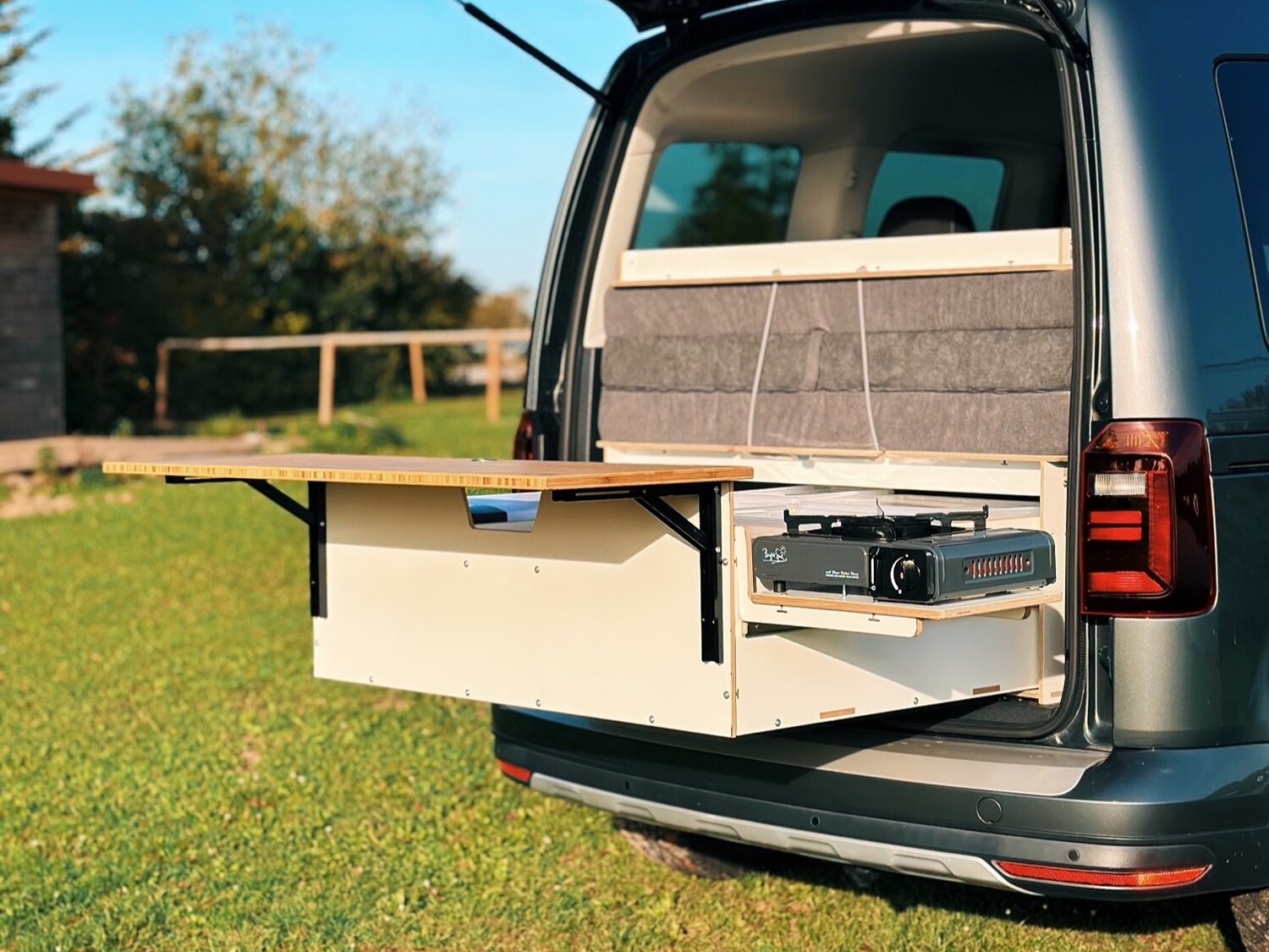 Moduł kuchenny z rozkładanym stołem i kuchenką gazową, który jest ustawiony z tyłu pojazdu.