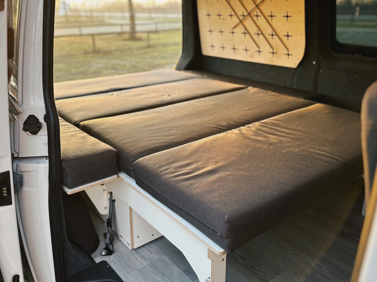 A comfortable sleeping system for camping vehicles, consisting of several mattresses arranged in a van and bathed in soft light.