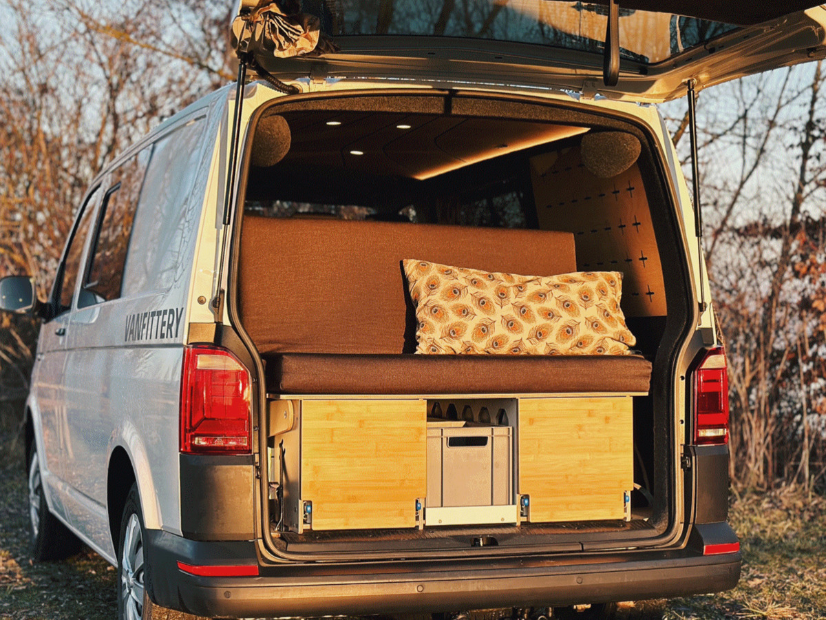 A converted camping van with a cosy sleeping area that offers an upholstered seat, a decorative cushion and practical storage solutions.