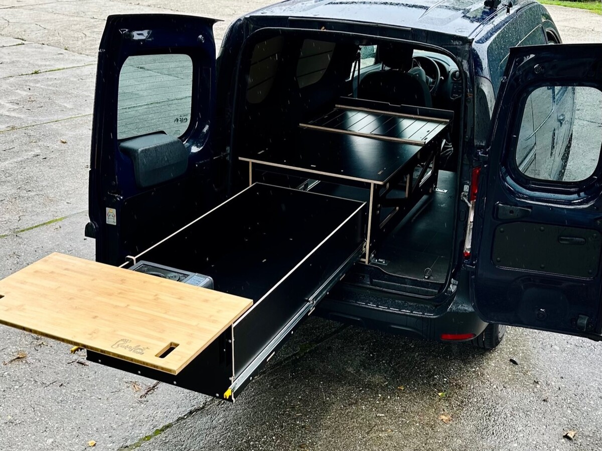 Un modulo da campeggio con sistema di cassetti estraibili viene presentato fuori da un veicolo, ideale per un'attrezzatura flessibile per dormire e cucinare all'aperto.