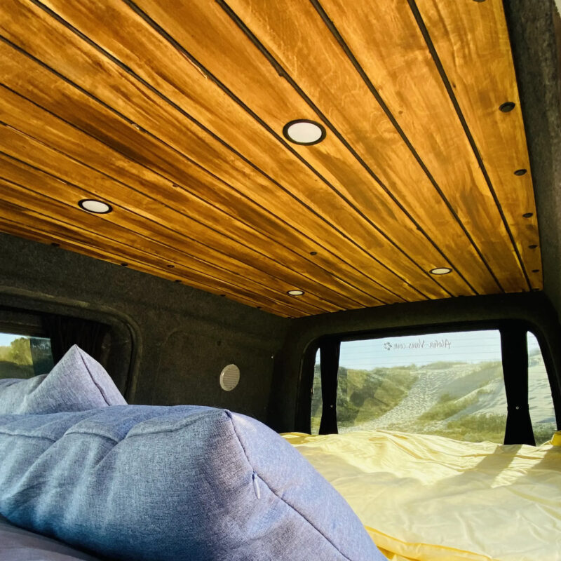 Interiér obytného vozidla s dřevěným stropem, útulnými polštáři a hřejivou atmosférou.