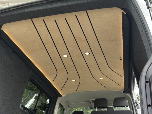 Widok wnętrza pojazdu kempingowego przedstawia stylowy drewniany sufit ze zintegrowanym oświetleniem LED i tapicerowanymi panelami ściennymi.