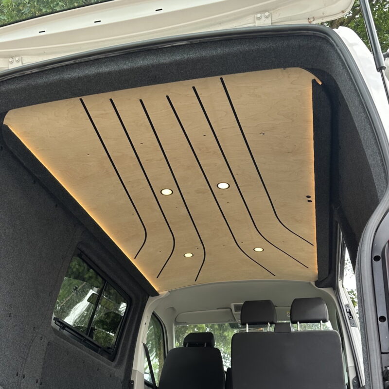 Pohled do interiéru obytného vozidla ukazuje stylový dřevěný strop s integrovaným LED osvětlením a čalouněné obklady stěn.