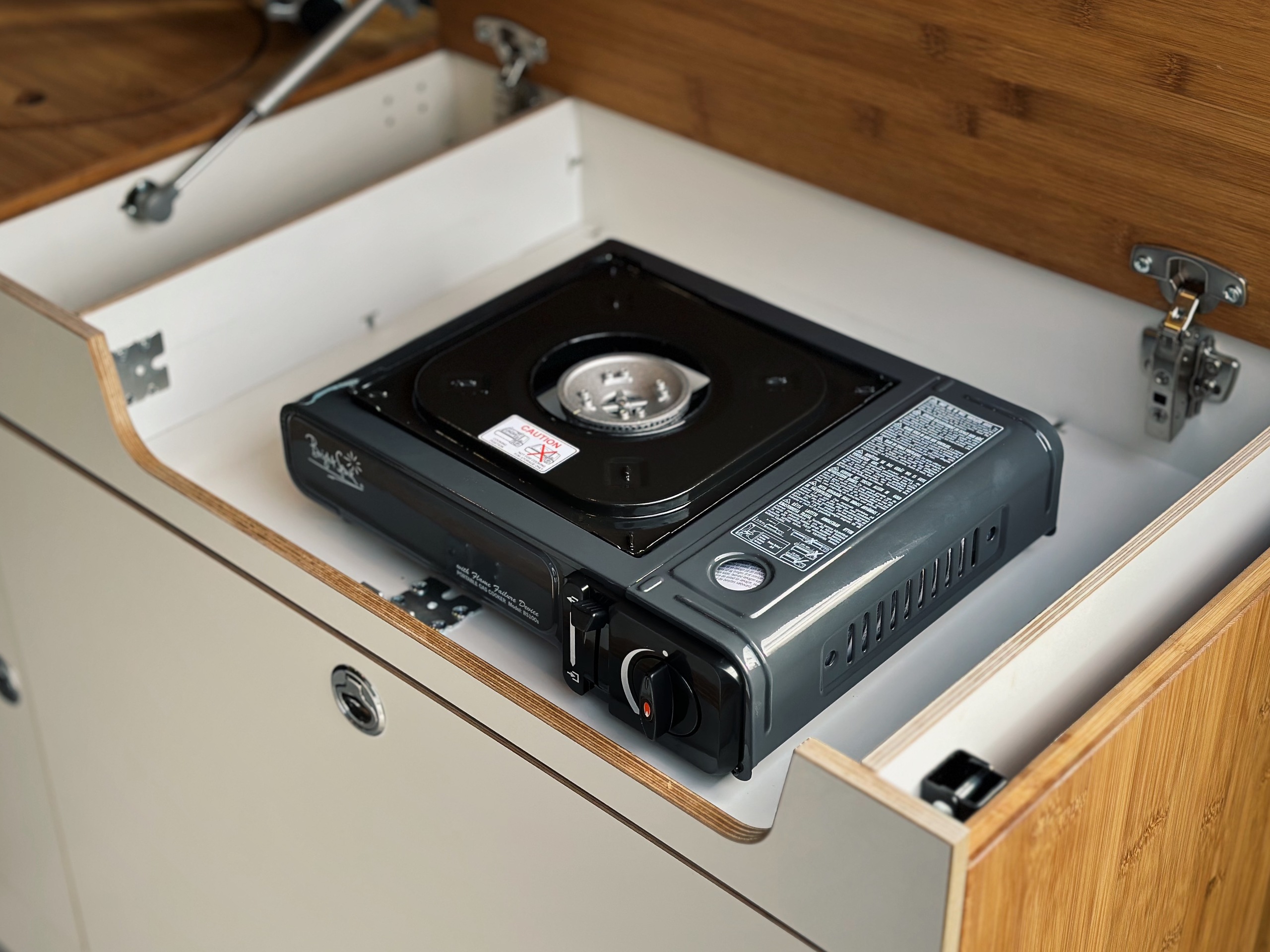 Přenosný kempingový vařič je integrován do kuchyňského modulu určeného pro venkovní použití.