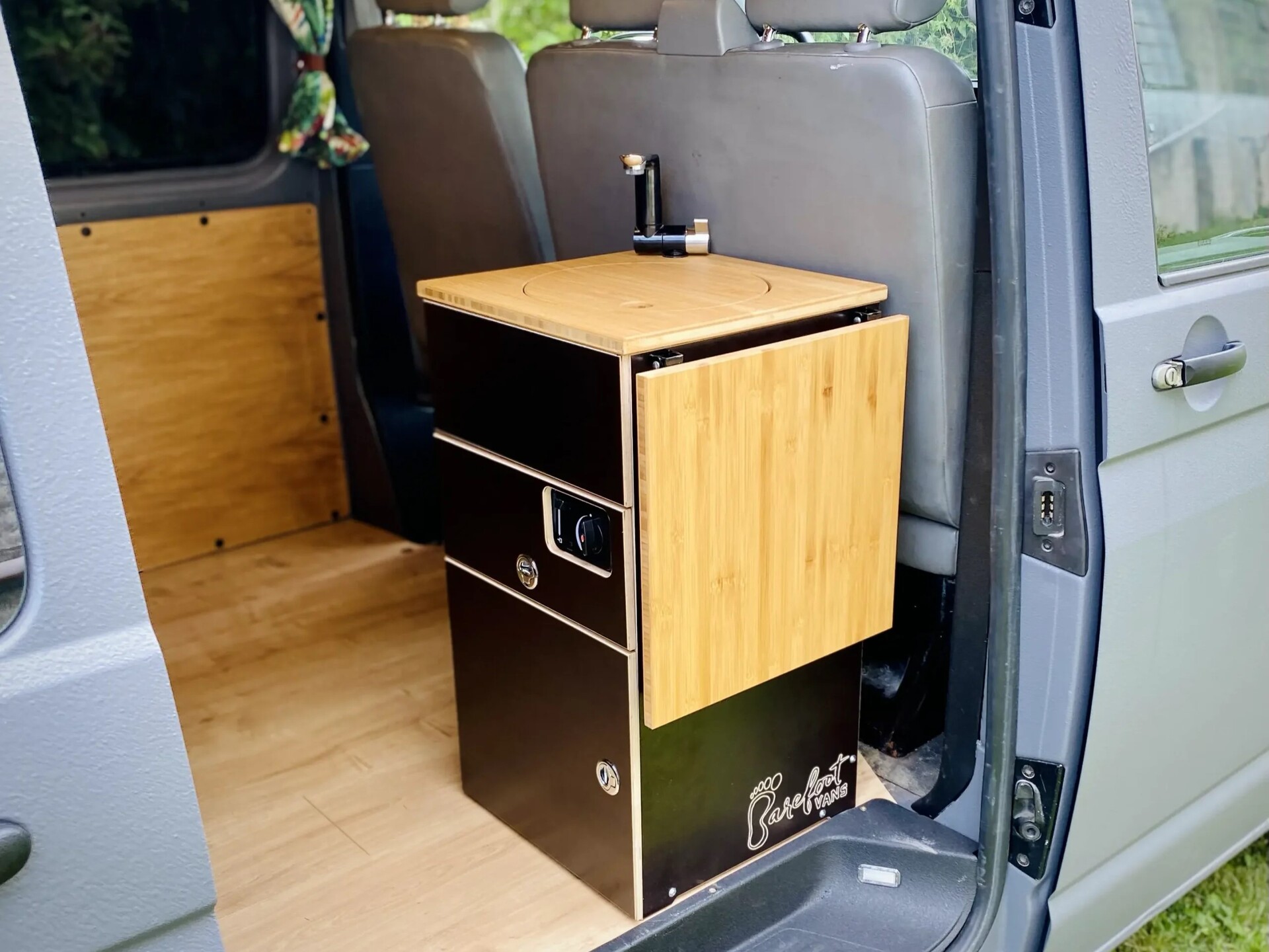 Et kompakt køkkenmodul til varevogne med træoverflade og praktisk opbevaringsplads, ideelt til camping og udendørs aktiviteter.
