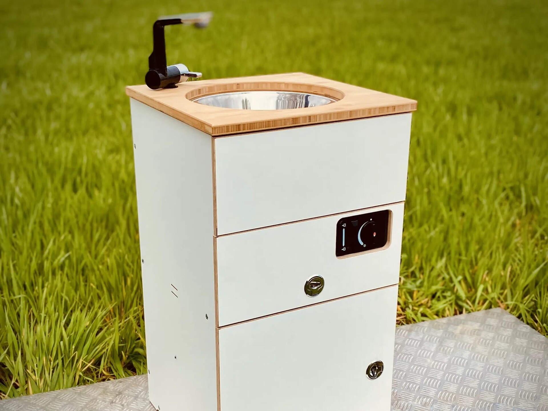 En moderne campinghåndvask med vask og vandhane i rustfrit stål, indbygget i et hvidt møbel med træoverflade og skuffer.