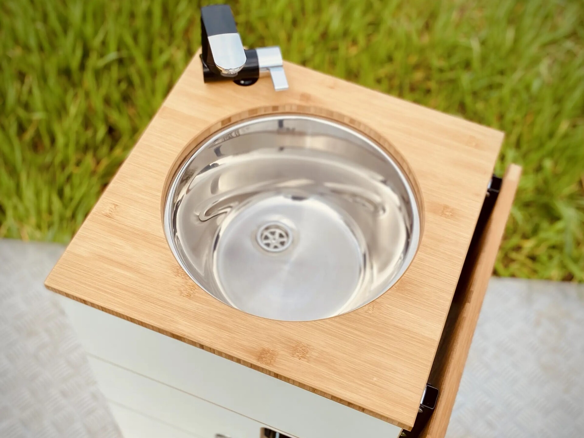 Nærbillede af et moderne campingkøkkenmodul med vask i rustfrit stål og træoverflade, ideelt til tilberedning af måltider i det fri.