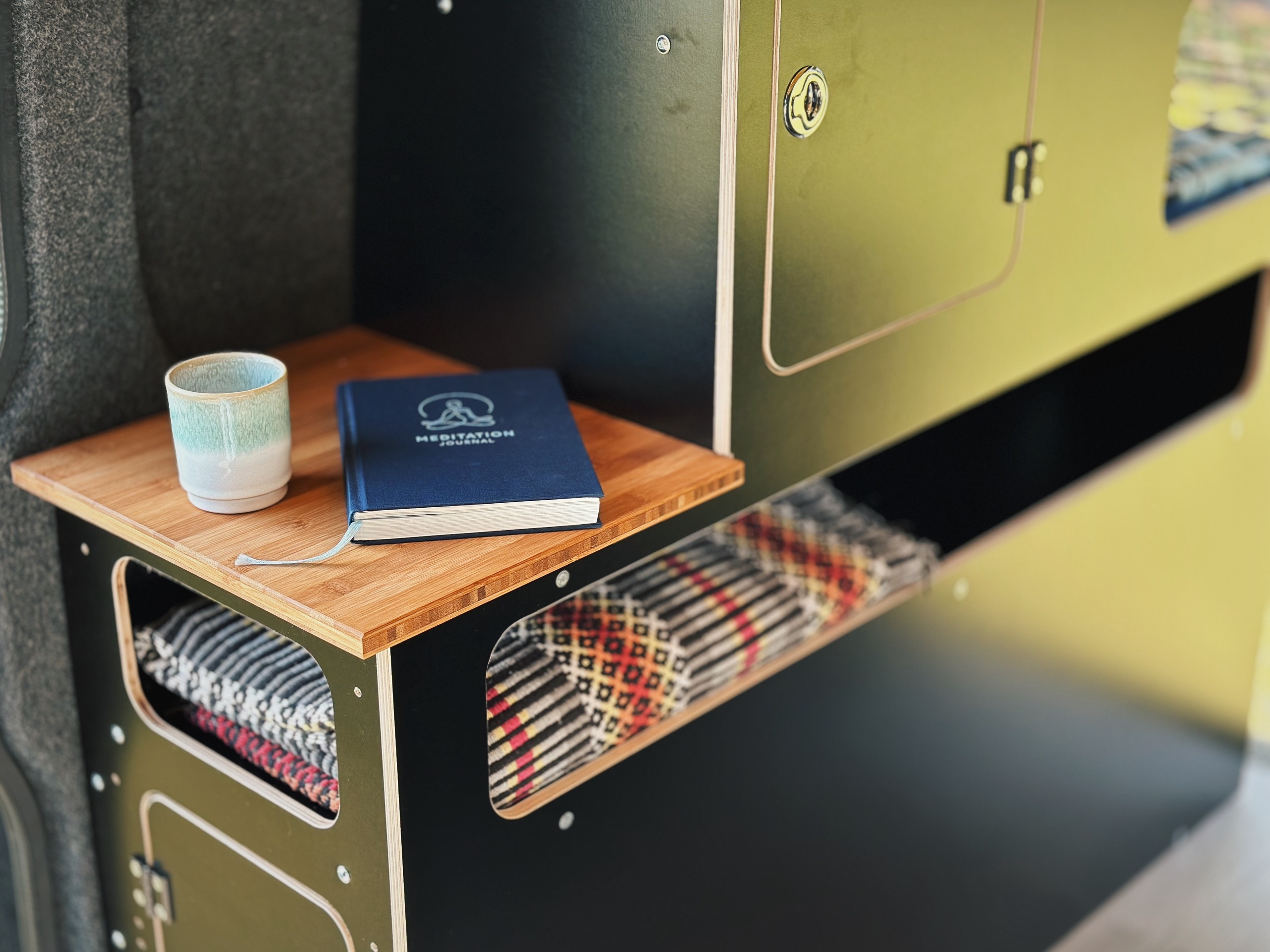 Modul kempinkového nábytku s dřevěnou policí, notebookem a skleničkou na povrchu.