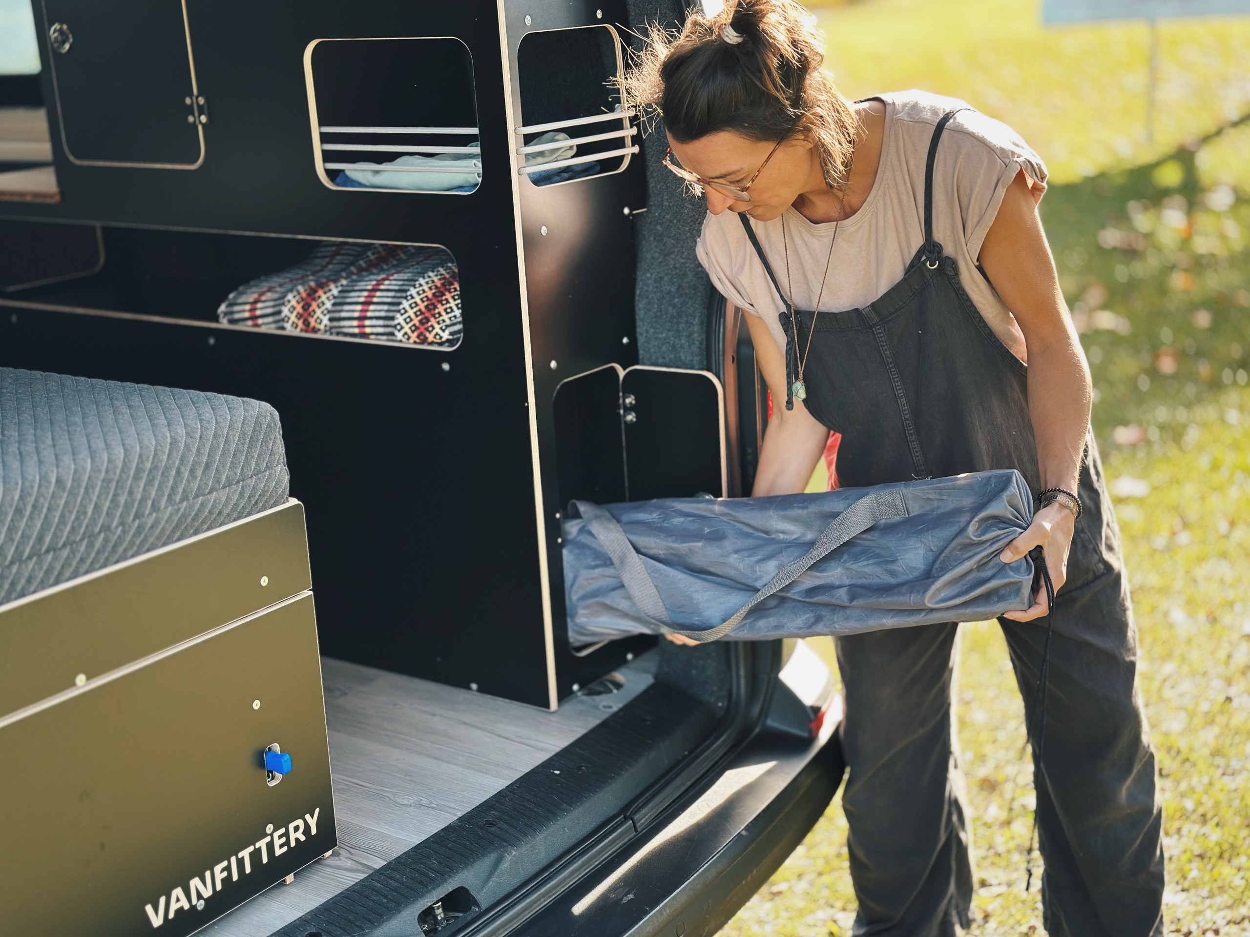 Osoba vyjímá deštník z mobilního skříňového modulu umístěného v autě, v pozadí je vidět zelená louka.